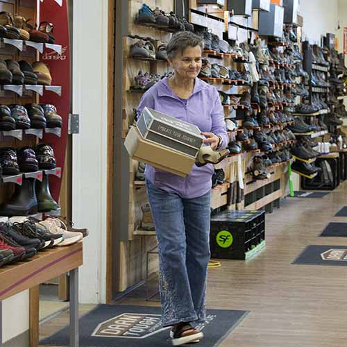 Woman holding a shoe in Farmway Vermont Gears Footwear Department